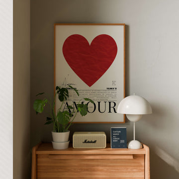 Framed heart poster with 'AMOUR' text on a wall above a wooden shelf with decorative items.